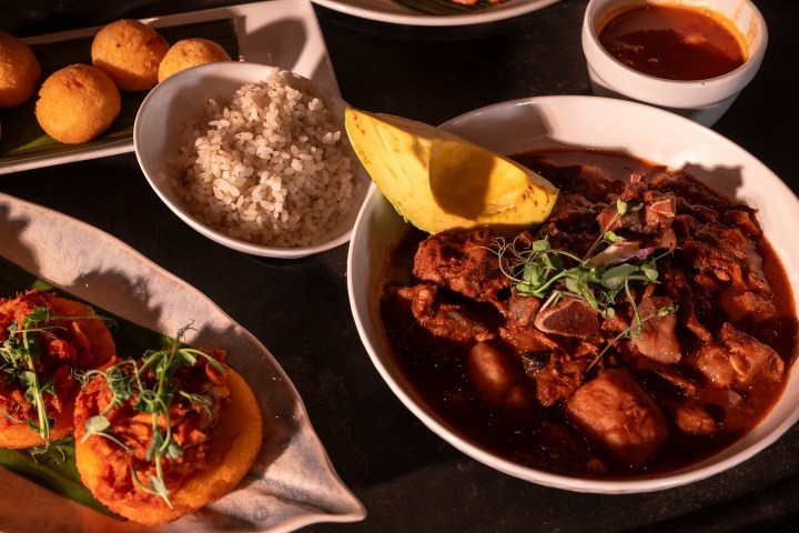 Assorted dishes including a beef stew, rice, cornbread balls, and a spicy garnish on a dark table.