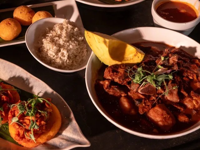 Harvest-Cook-image-1 Assorted dishes with meat stew, rice, fried balls, and topped toasts on a dark table.