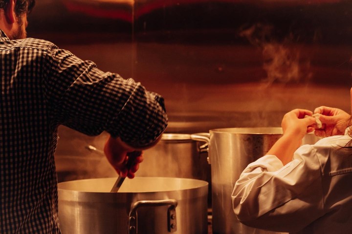 Two people cooking with large steaming pots in a kitchen.