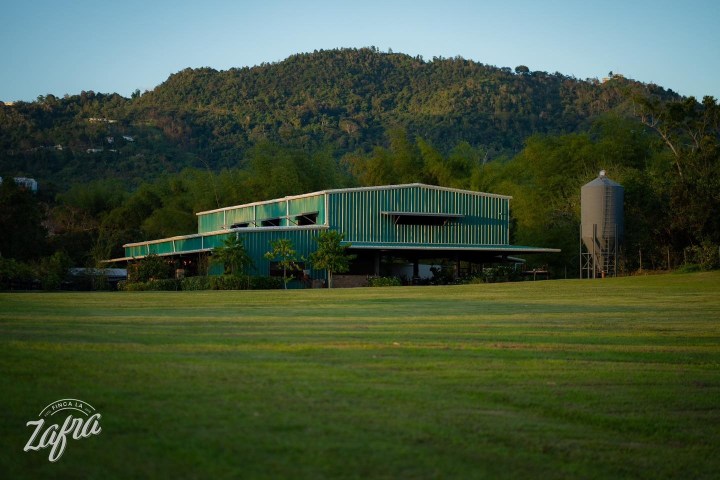 Green building with silo in lush landscape and mountain backdrop.