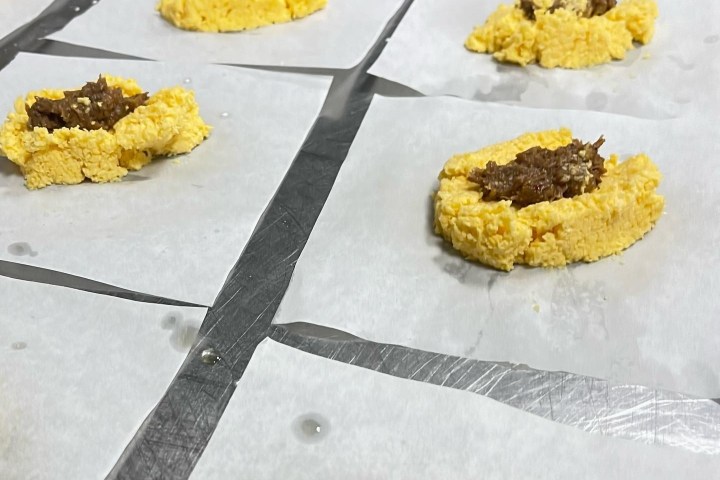 Unbaked dough with filling on parchment paper squares on a metal surface.