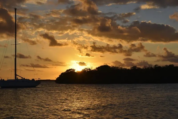 Silhouette of sailboat on water at sunset with cloudy sky.